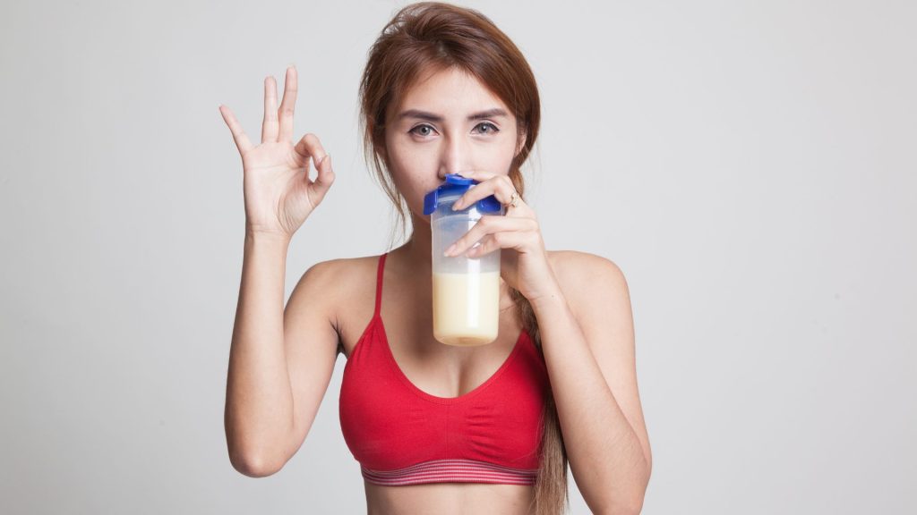 A woman drinking a protein shake and giving an OK sign